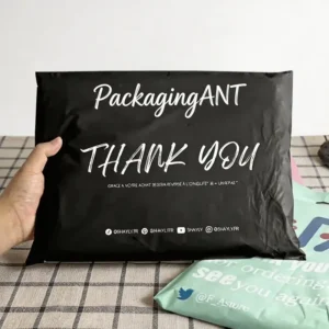 Hand holding a black poly mailer custom printed with white PackagingANT Thank You script