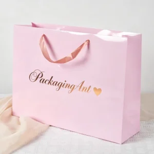 Single pink glossy gift paper bag featuring custom gold foil logo and matching pink satin ribbon handles.