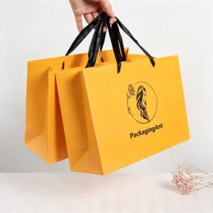 Hand holding a vibrant yellow custom shopping gift paper bag with black ribbon handles and black logo print.
