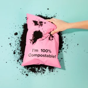 Pink 100% compostable bubble mailer resting in potting soil demonstrating home composting biodegradation