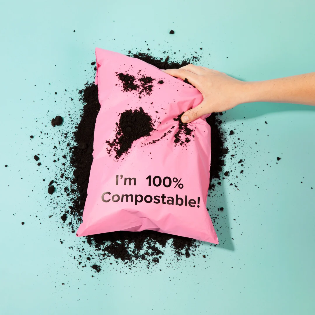 Pink 100% compostable bubble mailer resting in potting soil demonstrating home composting biodegradation