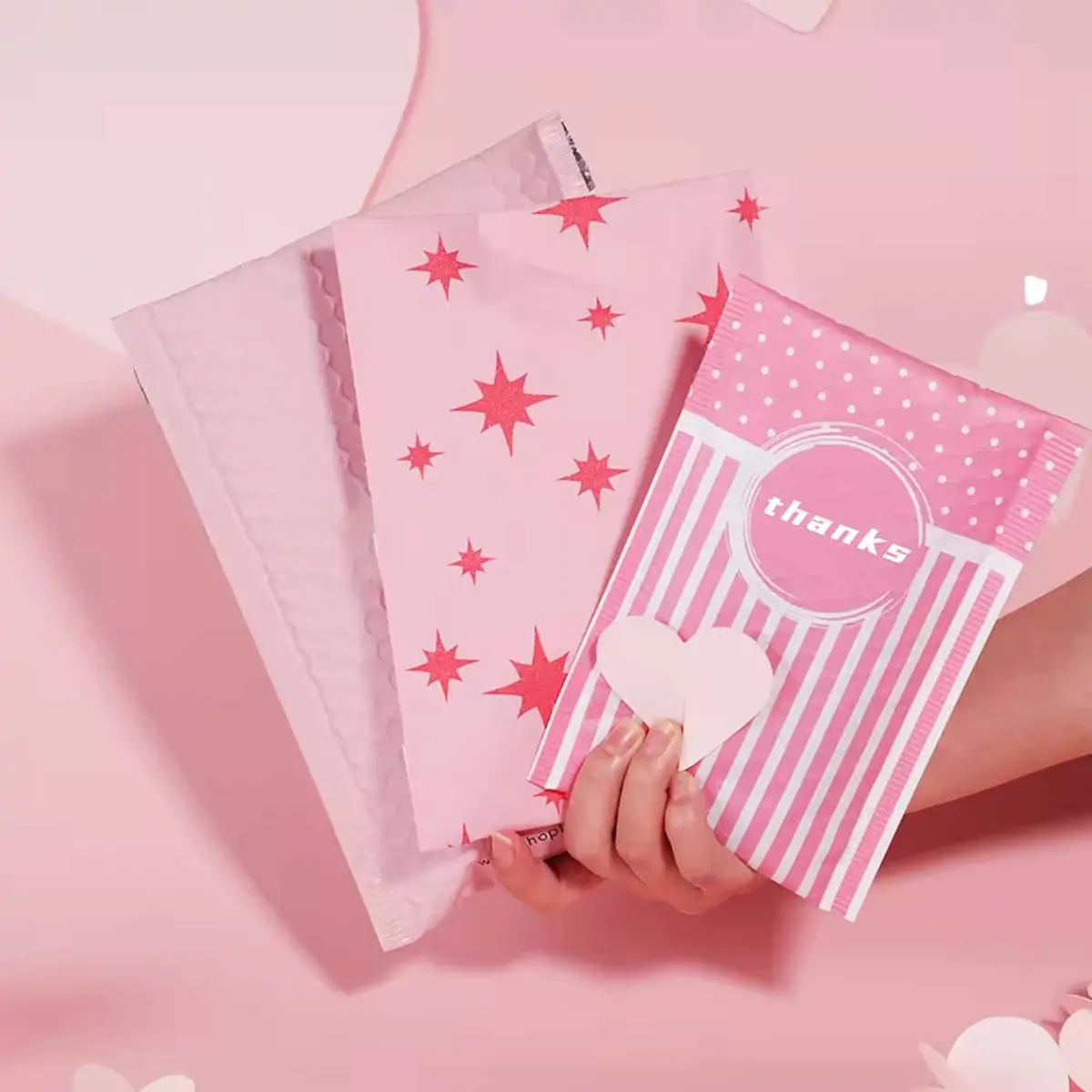 Custom printed pink recycled poly bubble mailers held in hand for boutique fashion e-commerce by PackagingANT