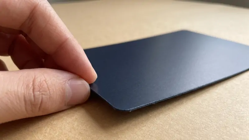 Close-up low-angle view of a thin dark navy card with anti-scratch matte lamination gently held by fingers